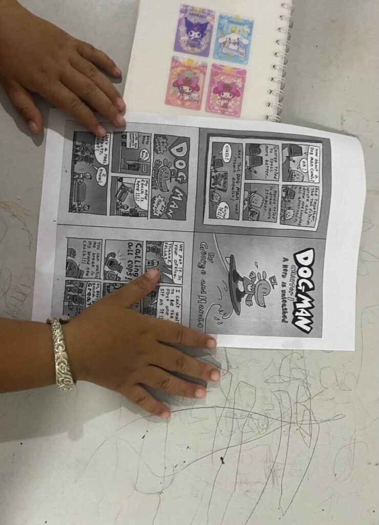 Close-up of a child's hands holding open a copy of a Dog Man graphic novel, reading the comic panels.